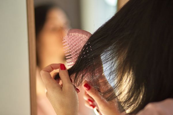 Trasplante de cabello en México; presentación de una mujer cepillándose el cabello frente al espejo mientras observa sorprendida la caída de su cabello.