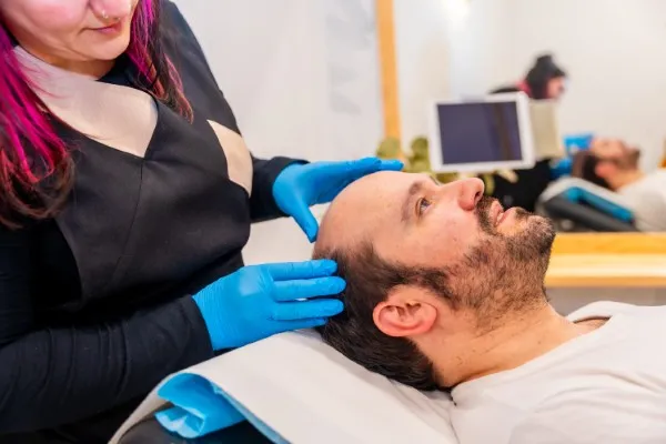 Dermatóloga examinando el patrón de calvicie de un hombre, paso crucial previo al tratamiento de injerto capilar en Cancún