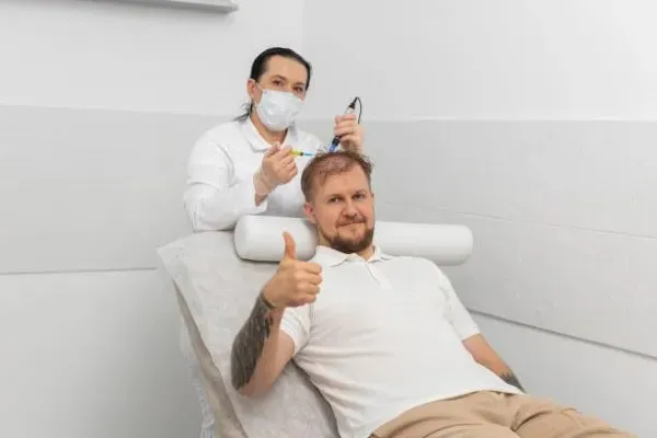 Médico realizando el trasplante de pelo con la técnica DHI capilar a un paciente que muestra su pulgar en señal de aprobación.