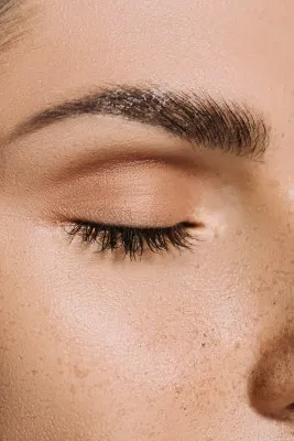 Macro view of a wet, freckled cheek and closed eyelid with a full, dark eyebrow, useful for comparing results and eyebrow hair transplant cost.