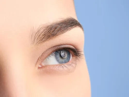 Profile view of a piercing light blue eye with dark lashes and a defined dark eyebrow on light skin, a distinct look related to eyebrow hair transplant cost.