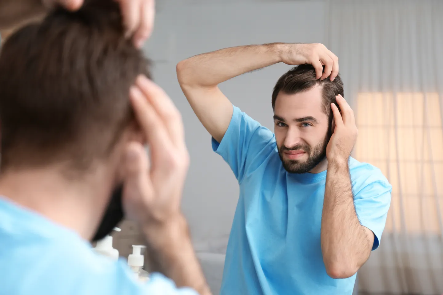 A young man looking in the mirror to check his hairline, asking does hair transplant leave visible scars.