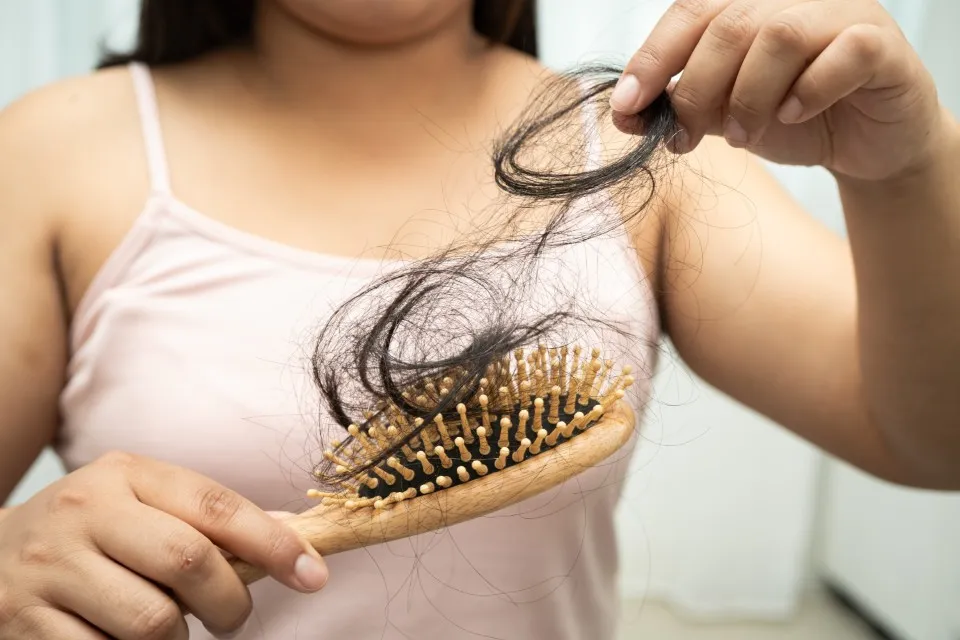 Close-up of a woman pulling a large clump of loose hair from a wooden brush caused by postpartum hair loss.