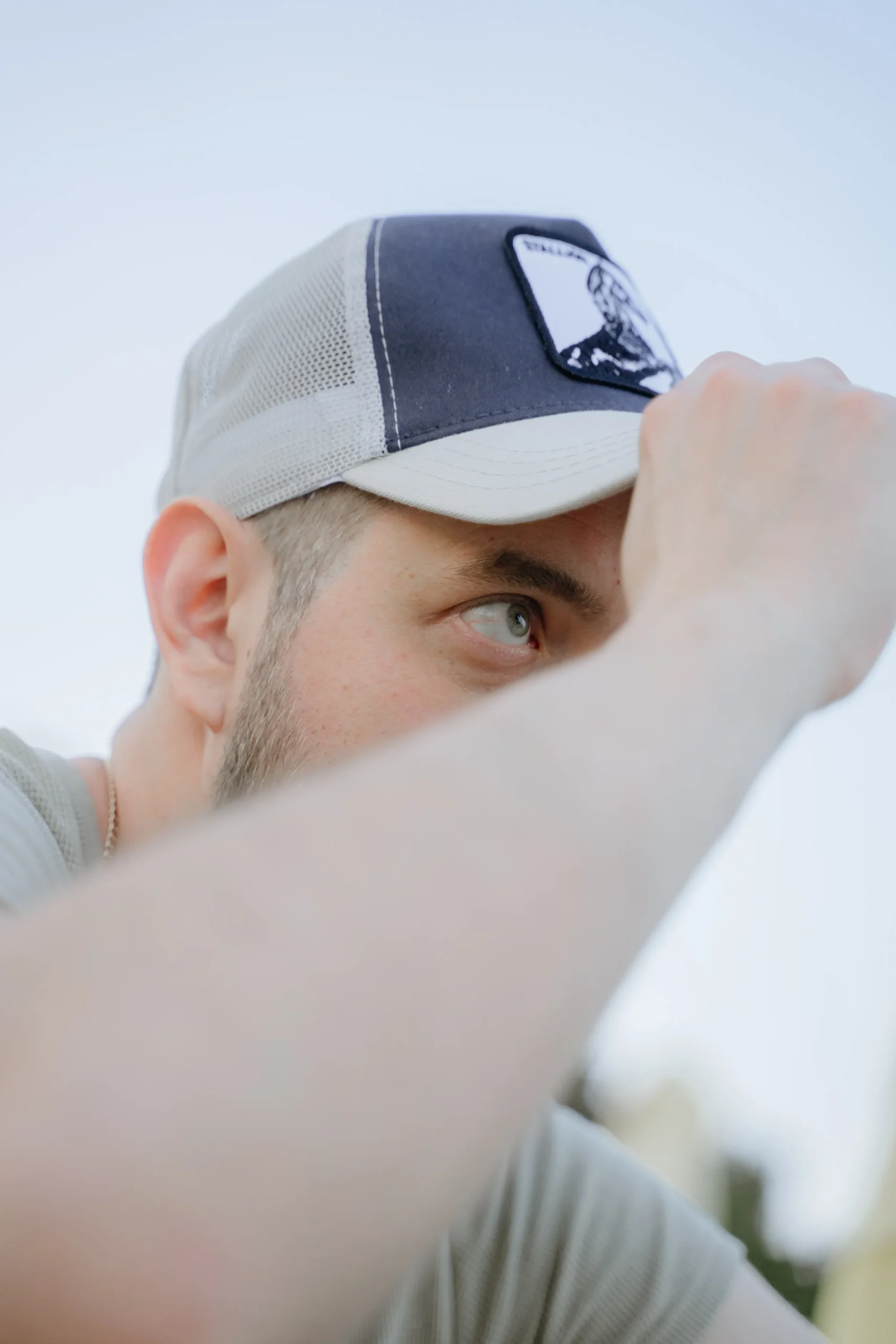 A smiling young man in a red shirt adjusts his cap. Can wearing hats cause hair loss or damage your hairline?