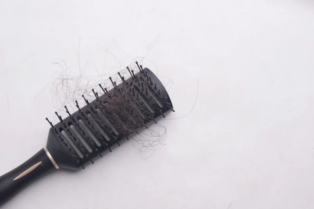 Black hairbrush filled with fallen strands of hair. Can wearing hats cause hair loss and severe thinning problems?