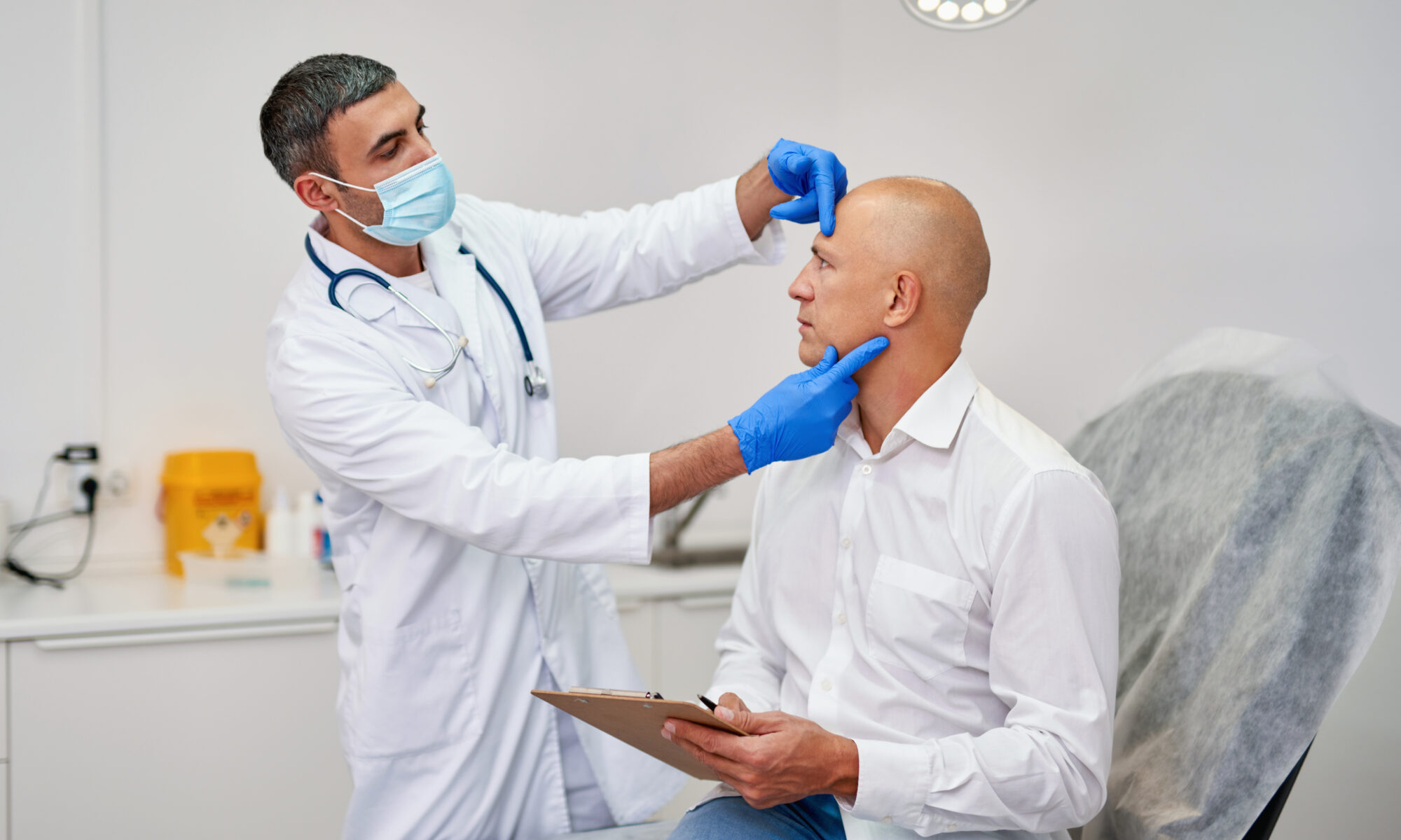 A doctor in a mask examines a man's bald scalp during a consultation to discuss "does hair transplant hurt".