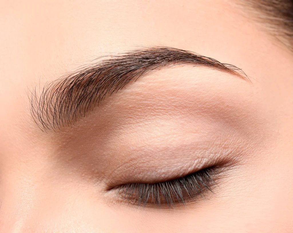 Macro view of a closed eye and perfectly groomed brow hairs, ideal results of an eyebrow hair transplant.