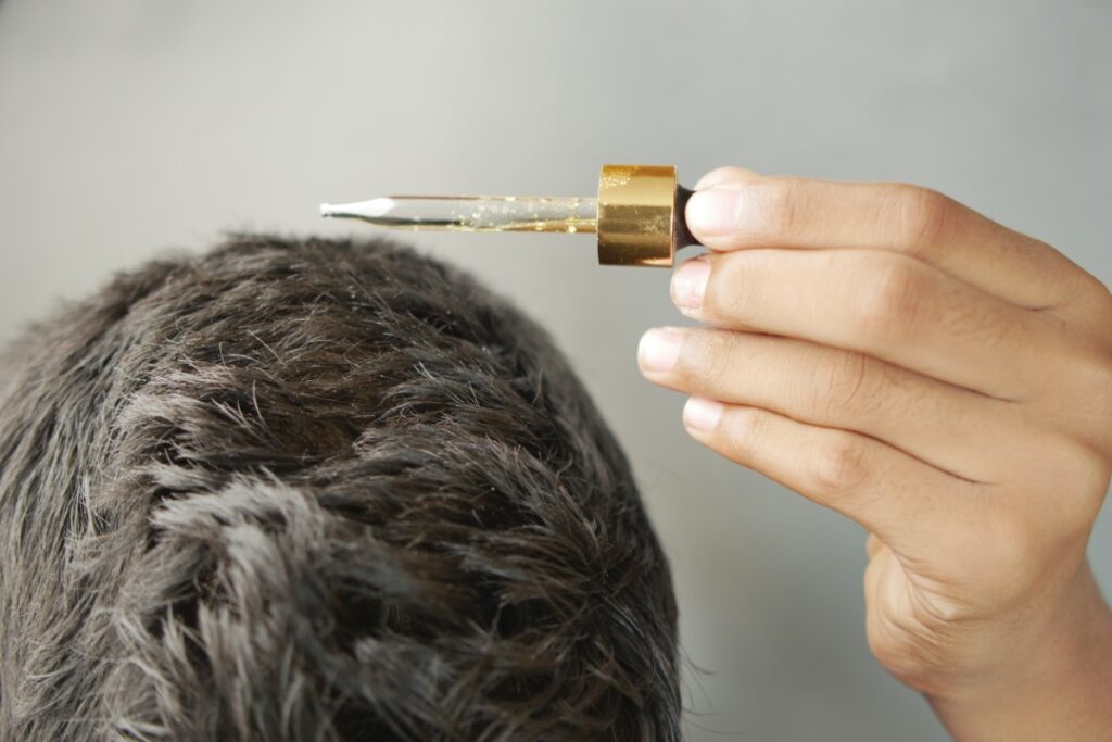 Hand with a dropper applying nutrient-rich oil, which could contain hair growth peptides, to a person's scalp.