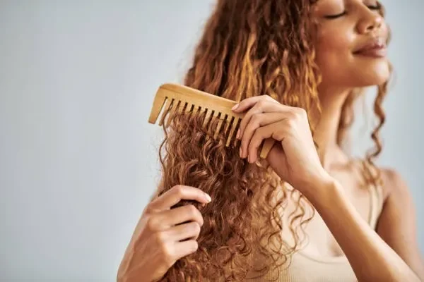 A young woman with curly hair styling her waves carefully in front of a mirror to maintain bounce and volume, embracing a Healthy way to grow hair fast.