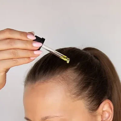 Woman applying nourishing serum to her hair as part of a routine that complements foods that strengthen hair for better hydration and growth.