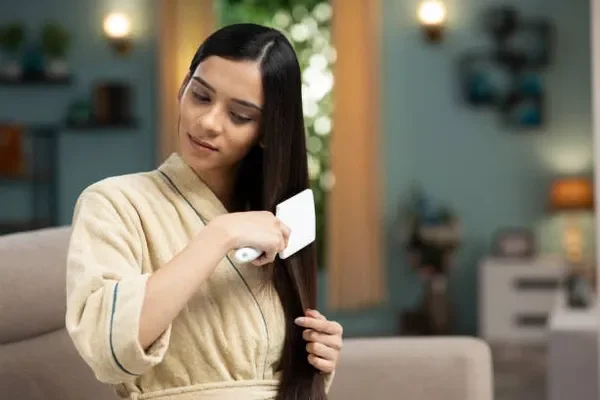 A woman with straight, shiny hair brushing it gently to reduce breakage and support a Healthy way to grow hair fast through daily self-care habits.