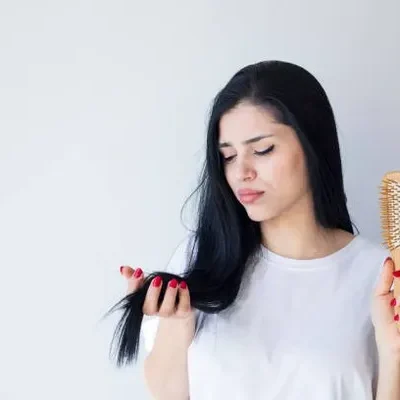 Woman brushing her long hair while seeing strands coming out on her brush, experiencing the normal shedding effect linked to new hair growth cycles.