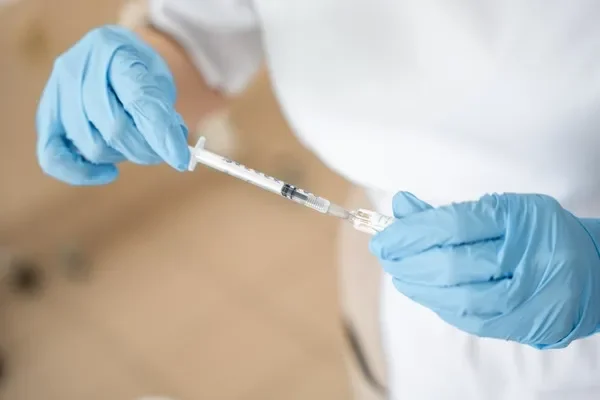 Primer plano de la mano de un médico llenando una jeringa con una solución de vacuna o anestésico antes de realizar una inyección profesional de botox capilar.