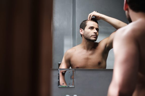 Young man in a bathroom concerned about premature hairline recession. Can you change your hair texture with a hair transplant?